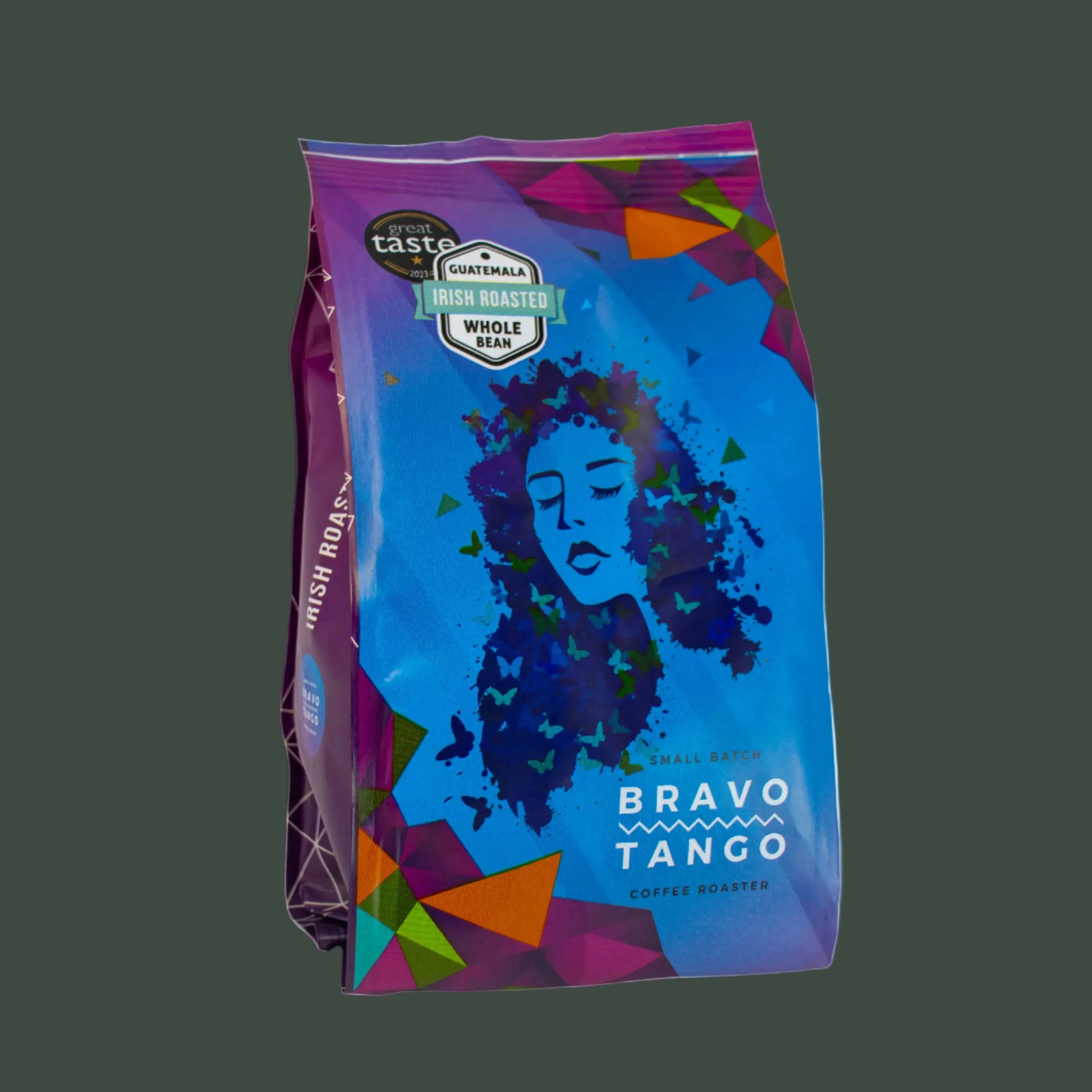 A bag of Brava Tango coffee beans on a solid dark gray background. The packaging features a vibrant blue and purple design with a stylized illustration of a woman's face and colorful geometric accents.