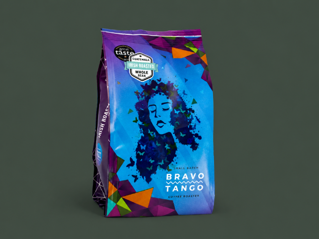 A bag of Bravo Tango Coffee Roast whole bean coffee, featuring a vibrant blue and purple design with a stylized graphic of a woman's face made of dark blue leaves, set against a dark gray background.