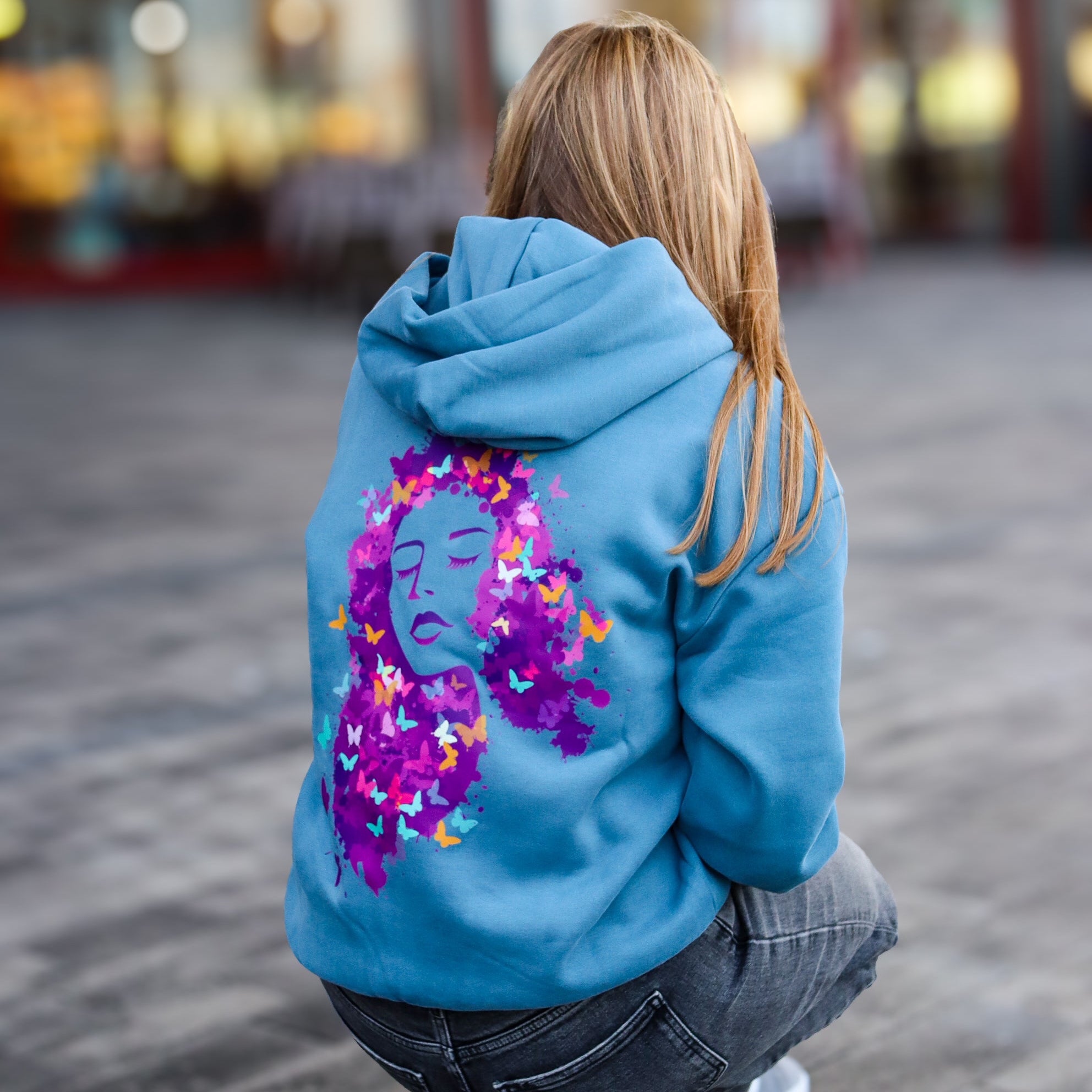 Person wearing a blue hoodie with a colorful design on the back, walking away from the camera.